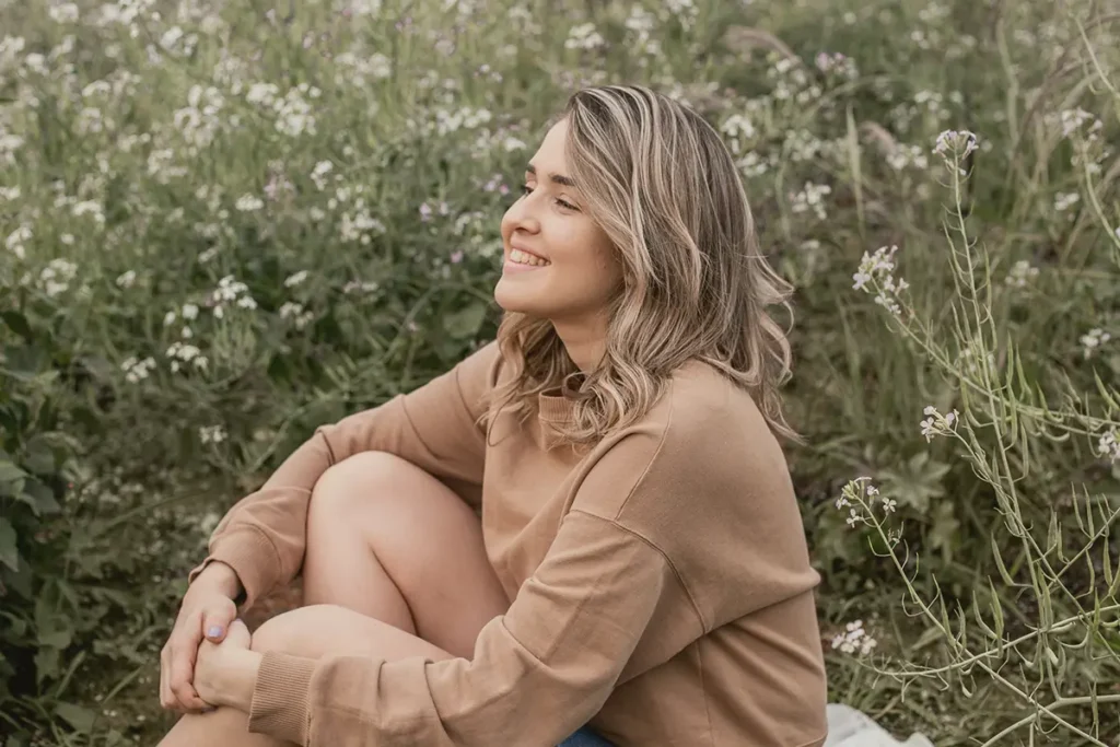 A woman in brown long sleeve shirt shitting on green grass during daytime