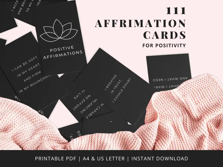 A set of black affirmation cards with white text arranged on a surface, beside a pink knitted fabric; card phrases include "I breathe trust, I exhale doubt.